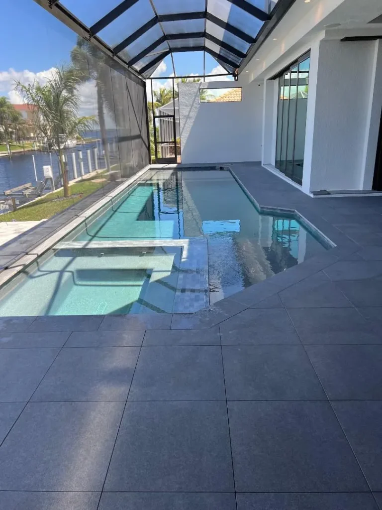 A modern lap pool with in-water loungers runs alongside a screened lanai overlooking a canal.