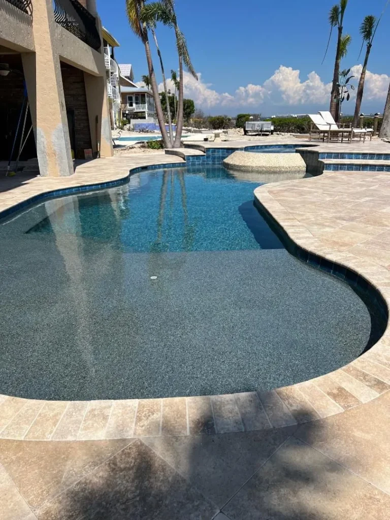 A freeform pool with a raised tiled spa and travertine deck under palm trees.