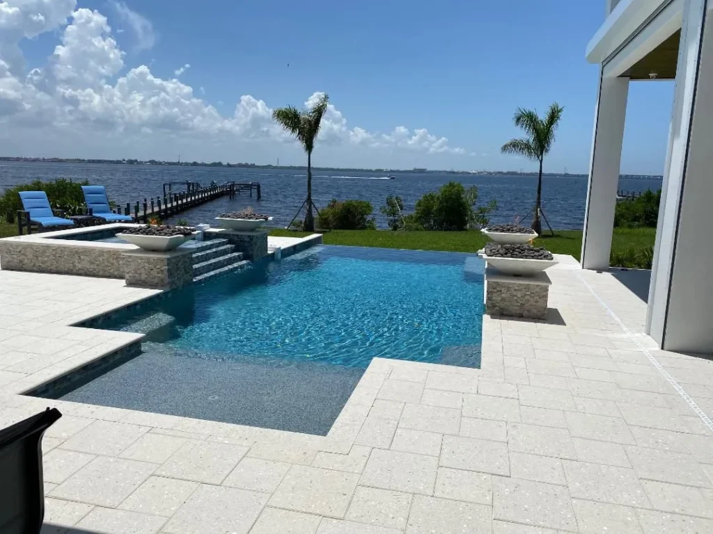 Infinity-edge style pool with raised spa, fire bowls, and travertine deck overlooking a wide waterway.