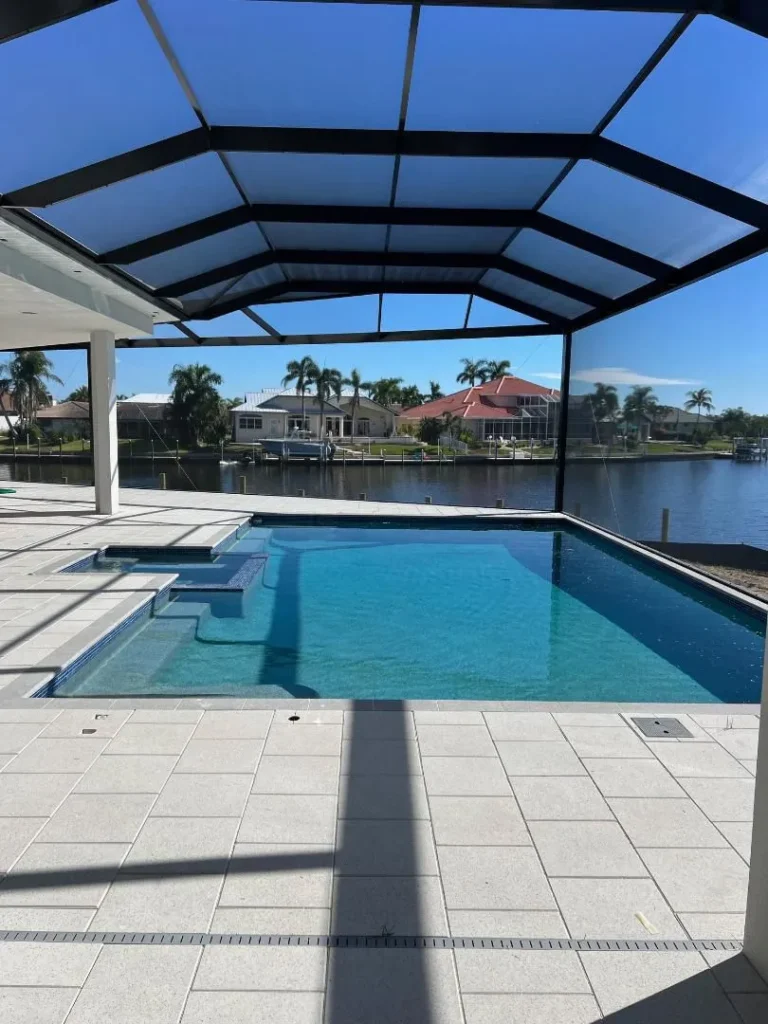 A rectangular pool with a screened enclosure overlooks a wide canal lined with waterfront homes.