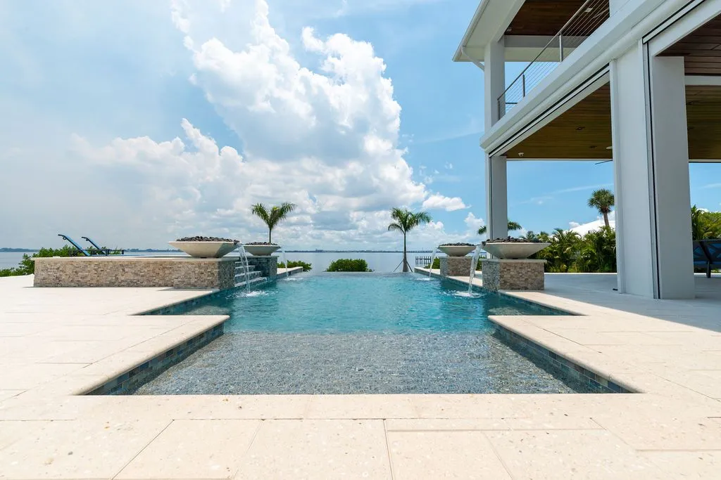 An infinity-edge rectangular pool with four spilling water bowls overlooks a bay from a modern waterfront home.