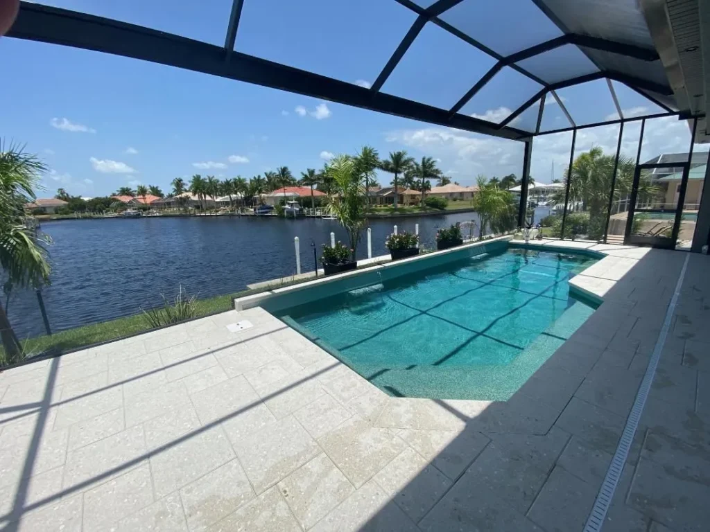 A screened lanai pool with a canal view lined with palm trees and waterfront homes.