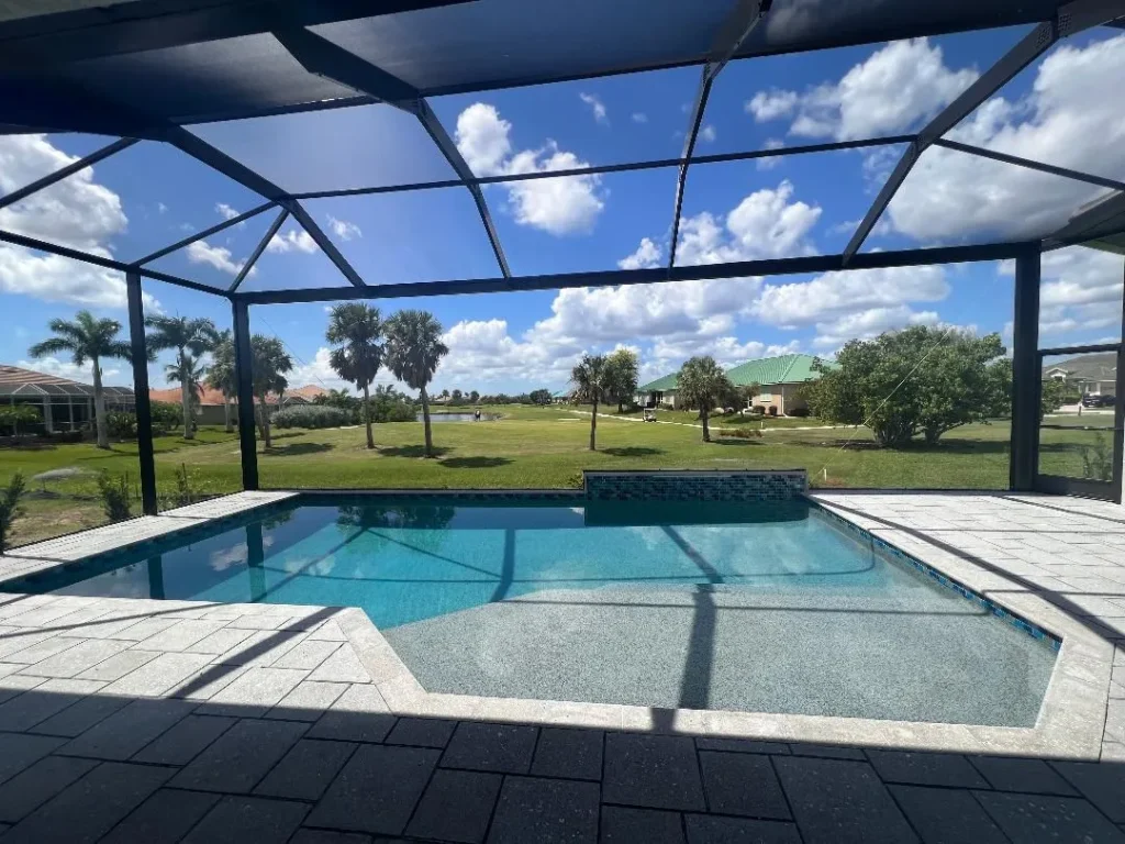 A screened backyard pool with a raised tiled spillway wall overlooking a golf course.