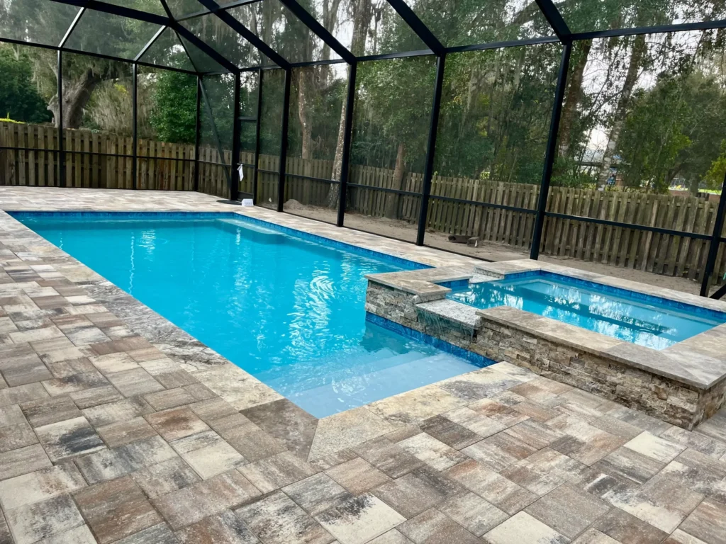 Rectangular pool with raised stone spa spilling over into pool under a screened enclosure.