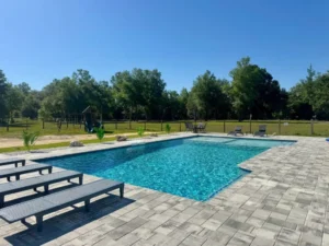 A rectangular backyard pool with a paver deck, loungers, and a play structure in the grassy yard beyond.