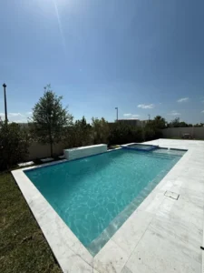 Rectangular backyard pool with raised spa and a low water-wall feature under a sunny sky.