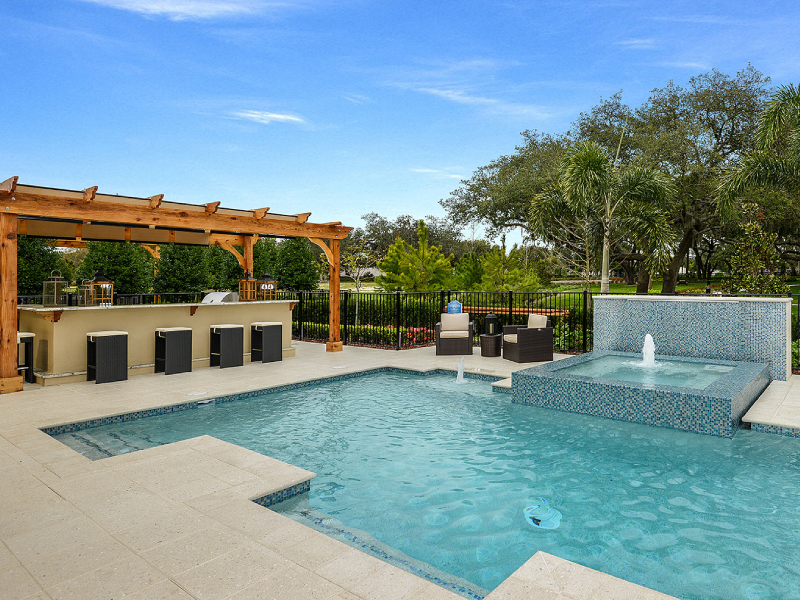 A geometric pool with a raised tiled spa spilling into it, next to an outdoor bar under a wooden pergola.