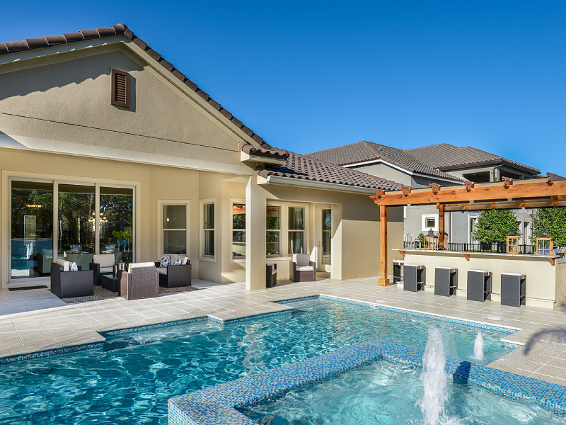A geometric pool with a raised spillover spa and bubbler fountain sits beside a covered patio bar and pergola.