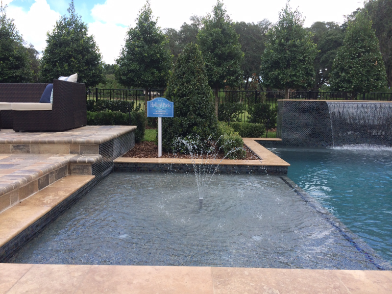 Corner of a geometric pool with a bubbler fountain and a tiled wall with a sheer descent waterfall.