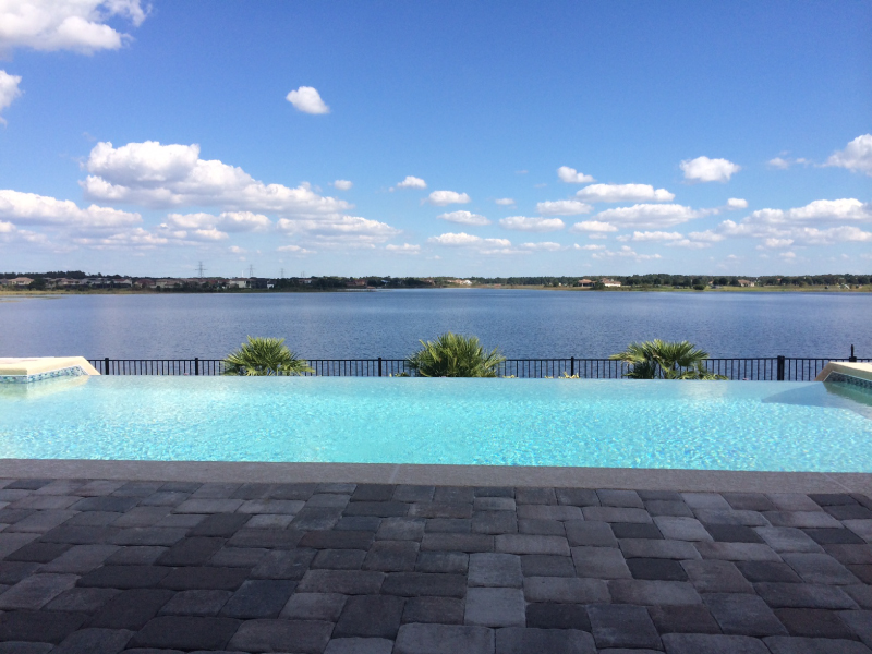 An infinity-edge pool overlooks a wide lake under a blue sky with scattered clouds.