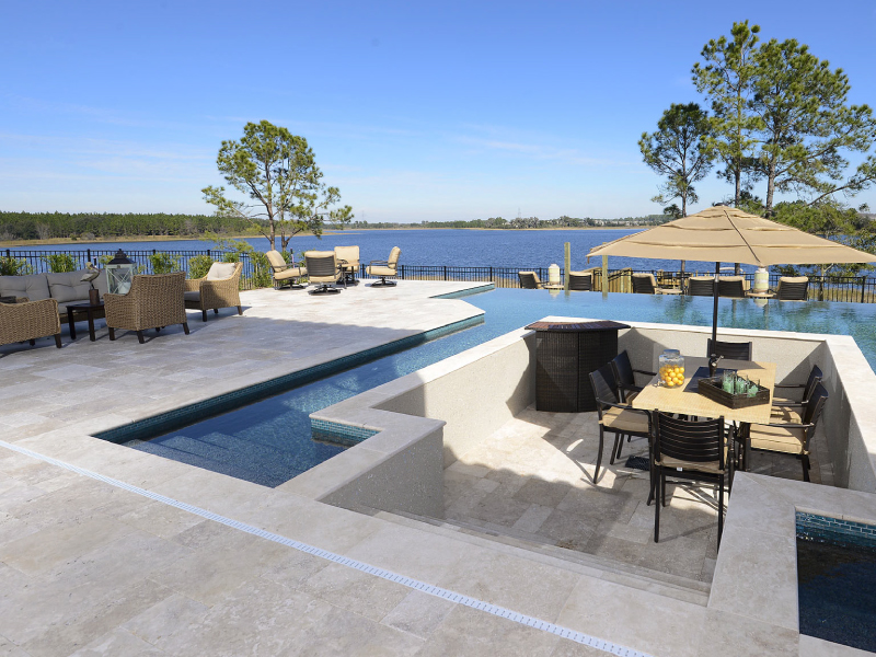 An infinity-edge pool with a sunken dining lounge overlooks a wide lake under an open sky.