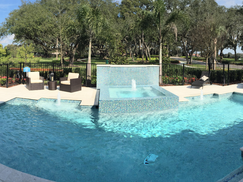 A freeform backyard pool with a raised tiled spa wall featuring water jets and spillover into the pool.