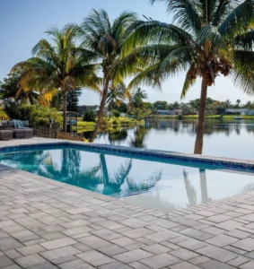 A rectangular pool with a vanishing edge overlooking a calm lake lined with palm trees.