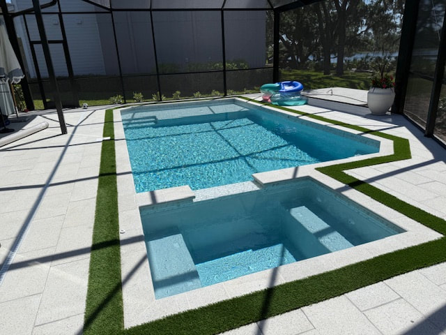 A rectangular pool with an attached spa at the same water level, enclosed in a screened lanai with turf-lined pavers.