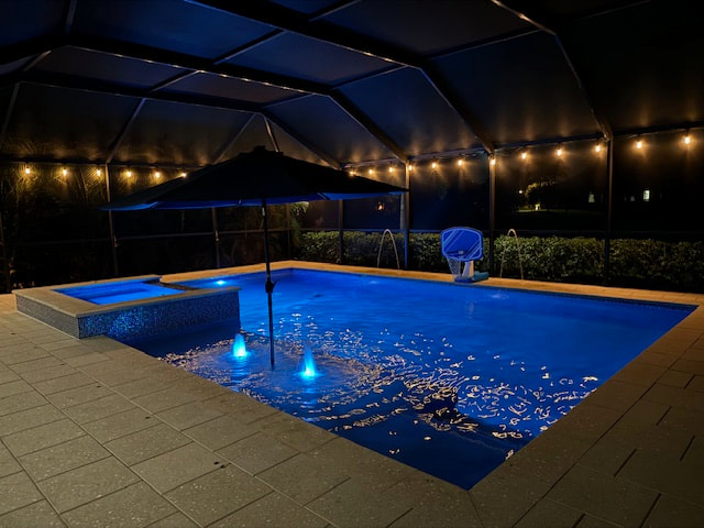 A screened backyard pool lit blue at night with a raised spa and string lights overhead.