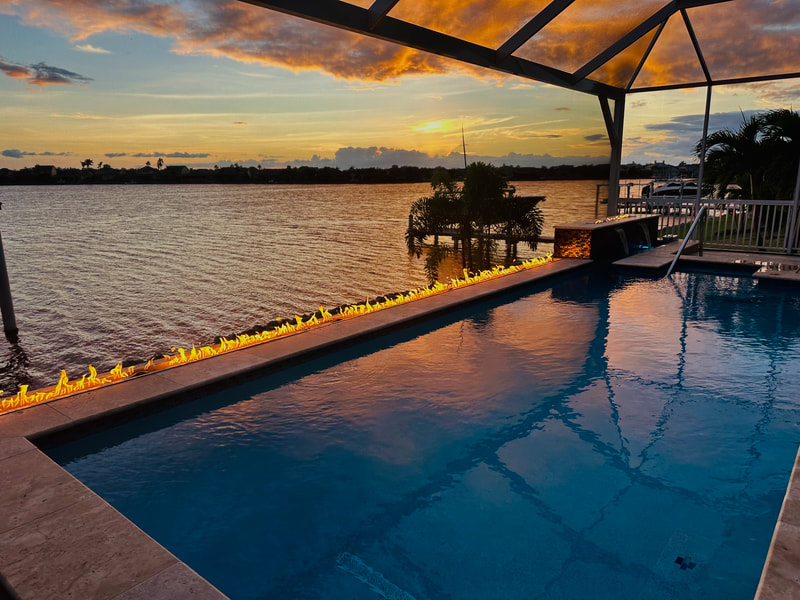 Infinity-edge pool at dusk with a long linear fire feature along the far edge overlooking a wide canal.