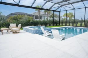 Rectangular pool with in-water lounge chairs and a raised blue-tiled spa under a screened lanai.