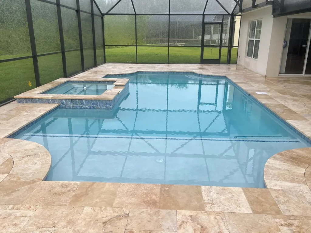 A rectangular gunite pool with a raised tiled spa under a screened enclosure with travertine paver decking.