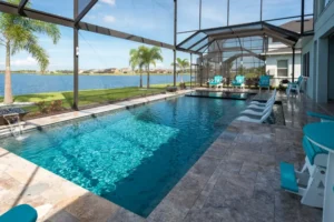 A long rectangular lake-view pool with in-water loungers under a screened enclosure.