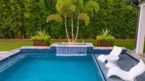 Rectangular backyard pool with a raised fire and water feature framed by palm trees and bamboo hedge.