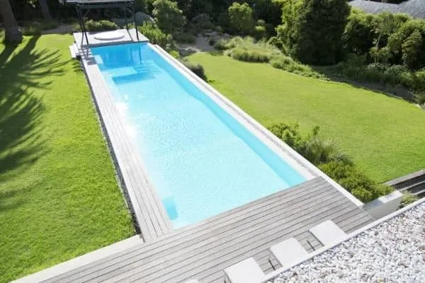 An aerial view of a long narrow lap pool with wood decking surrounded by lawn and a raised spa at one end.