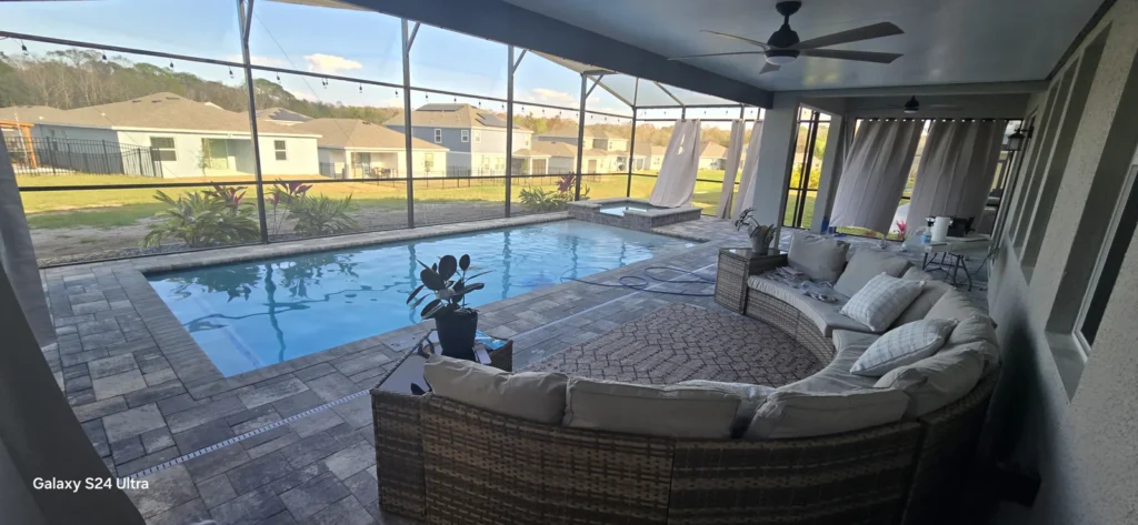 Rectangular pool with raised spa under a screened patio, phone watermark in corner.