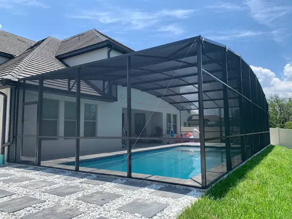 A small rectangular pool under a screened patio enclosure beside a house with a paver deck.
