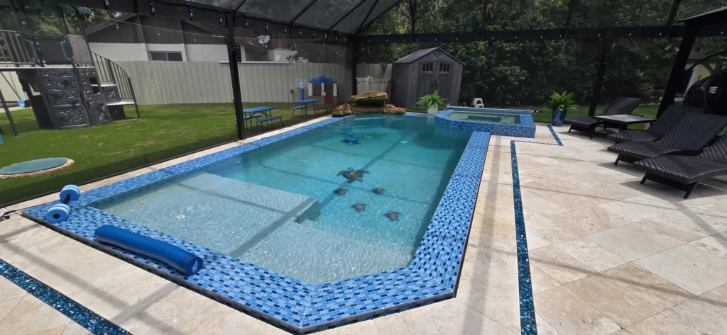A rectangular pool with mosaic tile trim and a raised spa sits under a screened lanai beside a travertine patio.