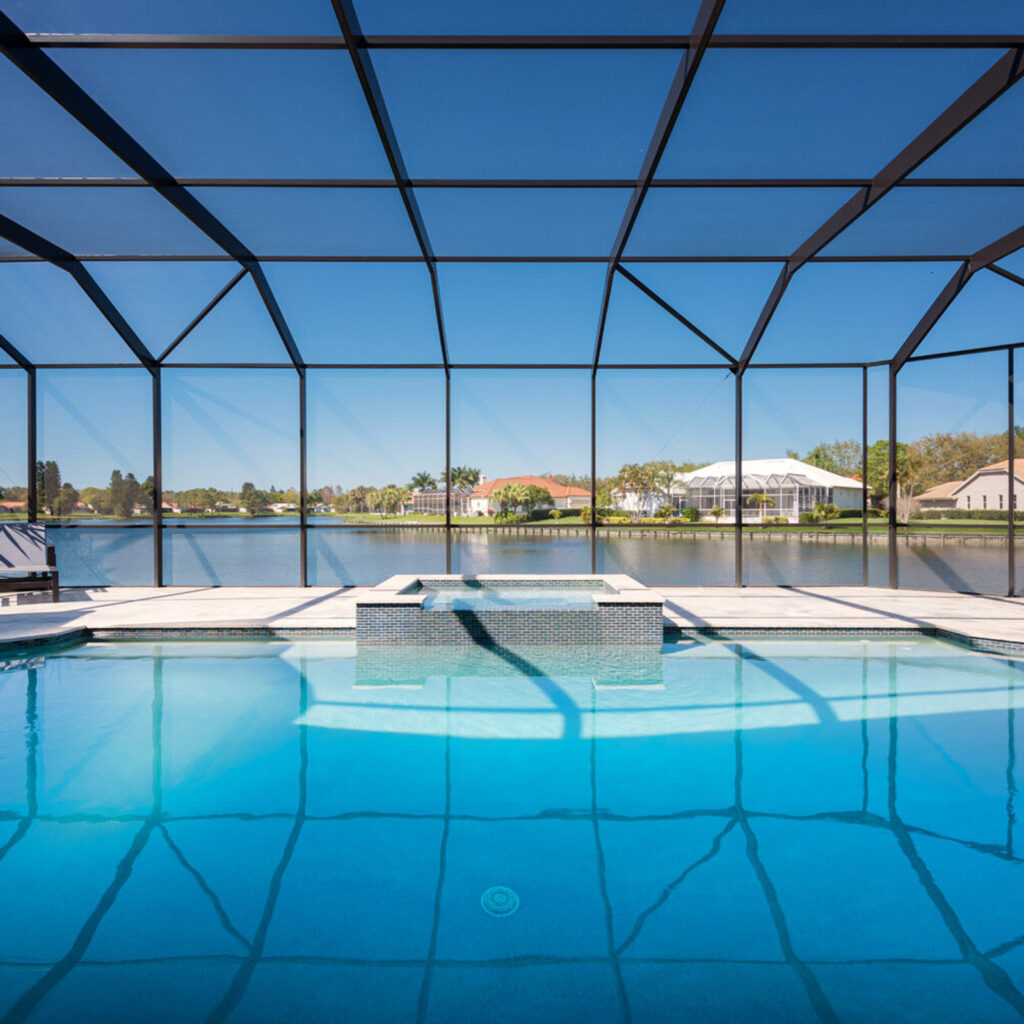A screened rectangular pool with a raised tiled spa overlooks a wide lake.