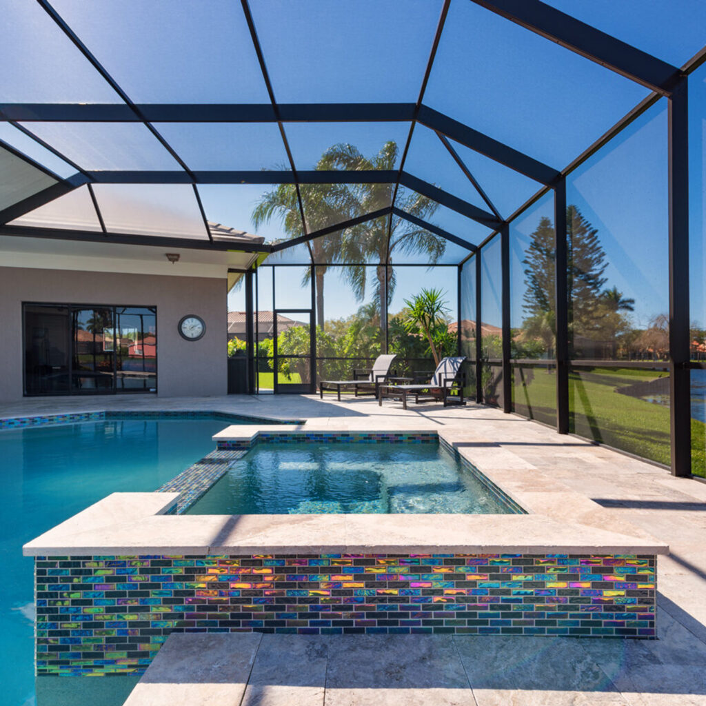 A raised spa with vivid iridescent glass tile sits beside a pool under a screened lanai overlooking a canal.