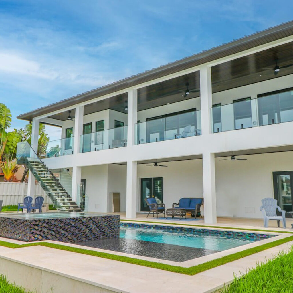 A modern two-story home with a rectangular pool and glass-tiled raised spa on a travertine patio.