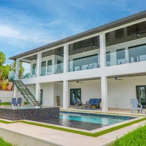 A modern two-story home with a rectangular pool and glass-tiled raised spa on a travertine patio.