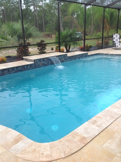 A small rectangular pool under a screen enclosure with a raised tiled wall and a water scupper feature.