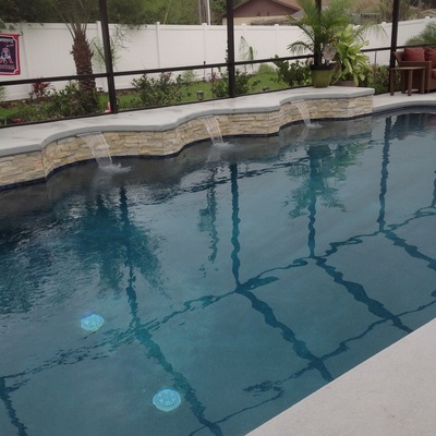 Freeform backyard pool with a curved stacked-stone wall and three scupper waterfalls under a screened enclosure.