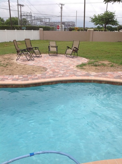 Freeform pool edge with a paver patio and outdoor chairs in a backyard.