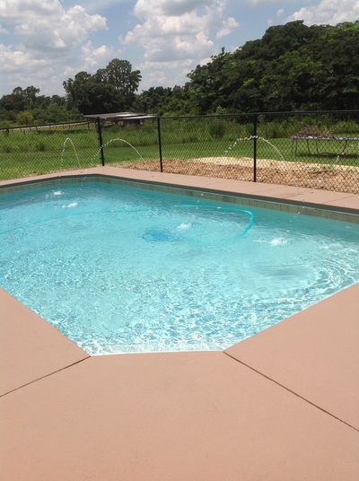 An octagonal vinyl-lined backyard pool with small deck fountains beside a rural fenced yard.