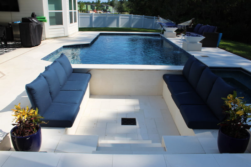 Rectangular pool with raised spa, water bowls, and a sunken navy sectional lounge on a travertine patio.