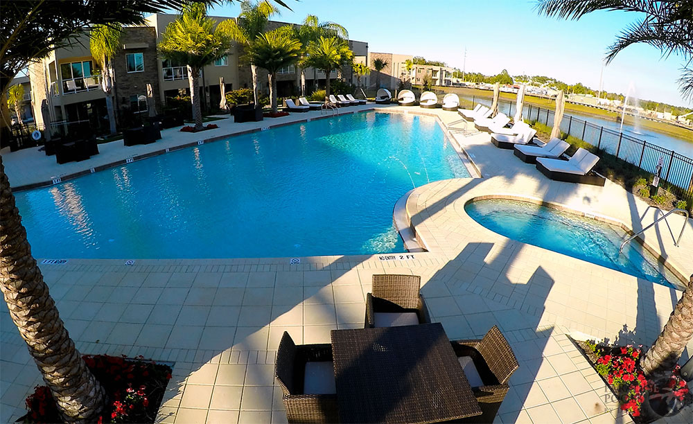A large freeform resort pool with an attached spa and rows of lounge chairs beside a lakefront apartment complex.