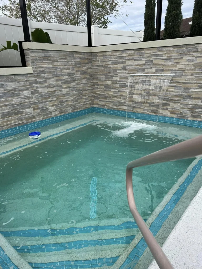 A small geometric plunge pool with a stacked-stone wall and sheet waterfall feature under a screened enclosure.