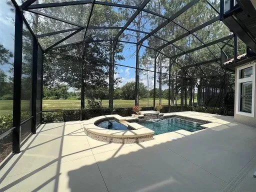 A small rectangular pool with a raised spa under a screened enclosure overlooking a grassy field.