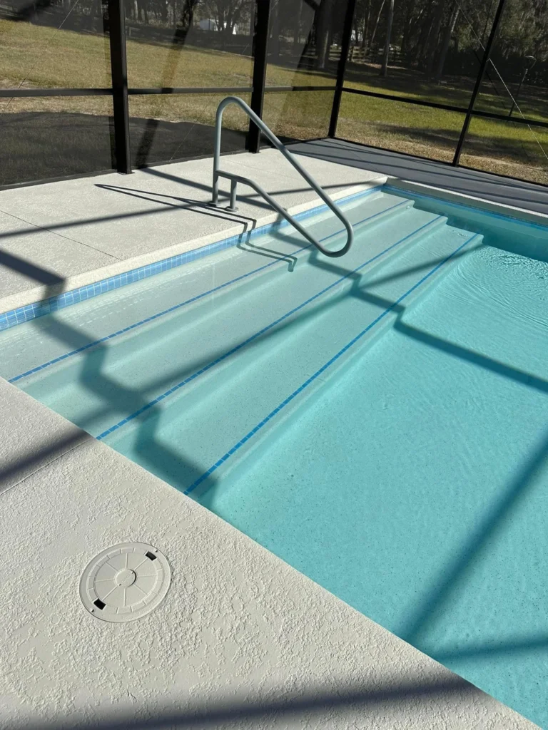 Corner view of pool entry steps with a handrail under a screened enclosure.
