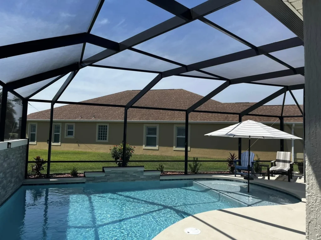 A screened-in freeform pool with a raised tanning ledge and stone accent wall in a suburban backyard.