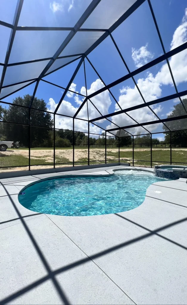 A freeform fiberglass pool with an attached raised spa under a large screened enclosure, open field beyond.