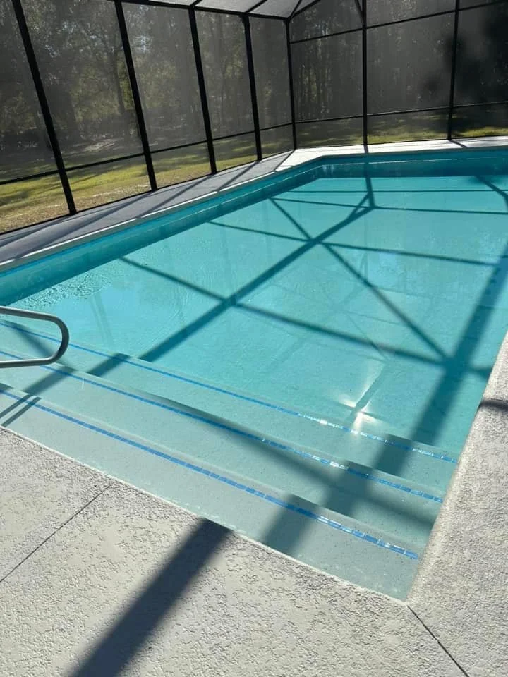 A small rectangular pool with tiled steps under a screened patio enclosure.