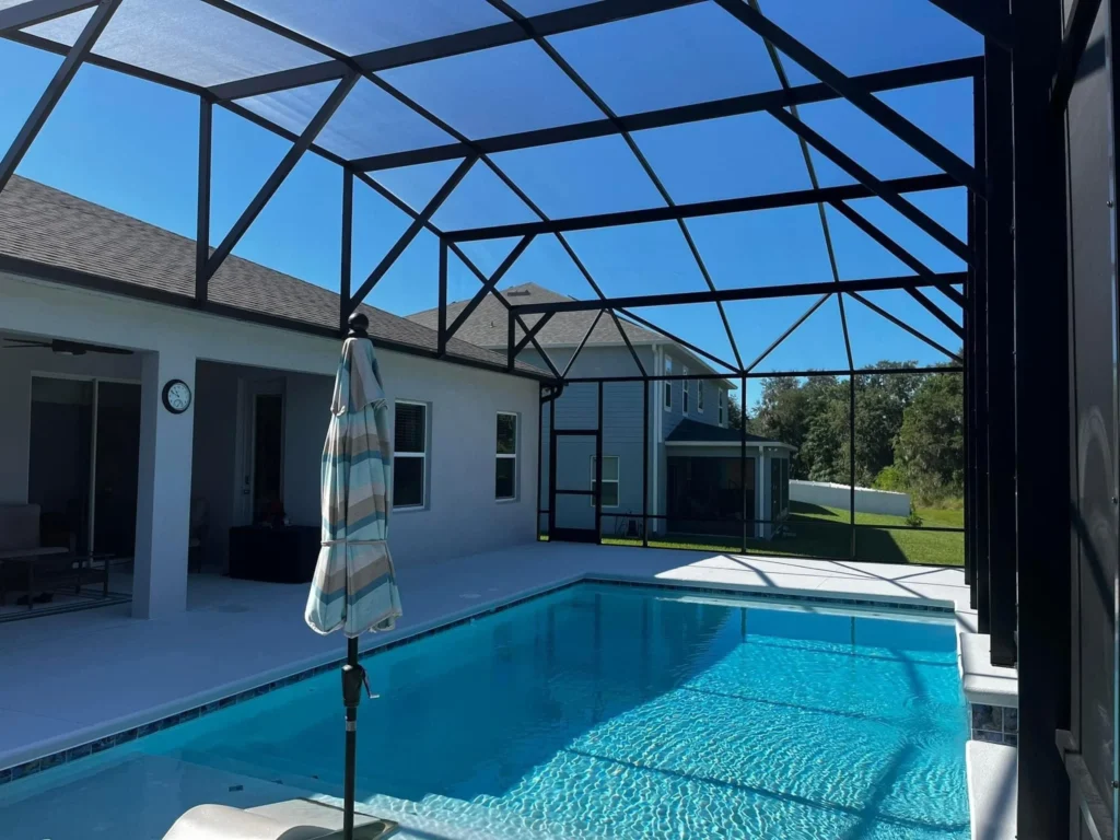 A rectangular pool under a screened lanai with a closed patio umbrella beside it.