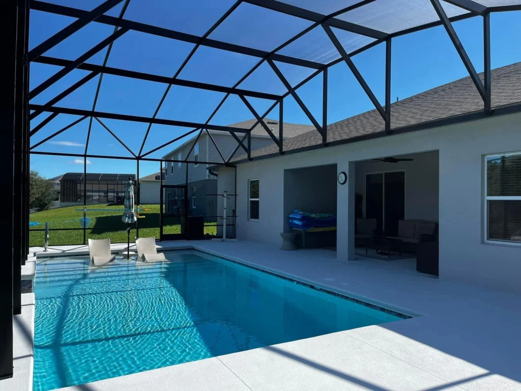A screened rectangular backyard pool with submerged lounge chairs next to a covered patio.
