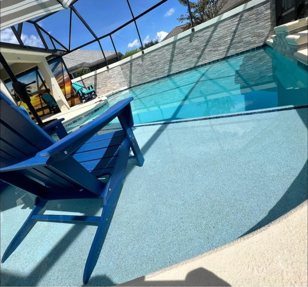A blue Adirondack chair on a textured pool deck with a screened lanai and stacked-stone wall beside the pool.