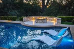 A rectangular pool at dusk with two floating loungers and a raised circular fire pit patio beyond.