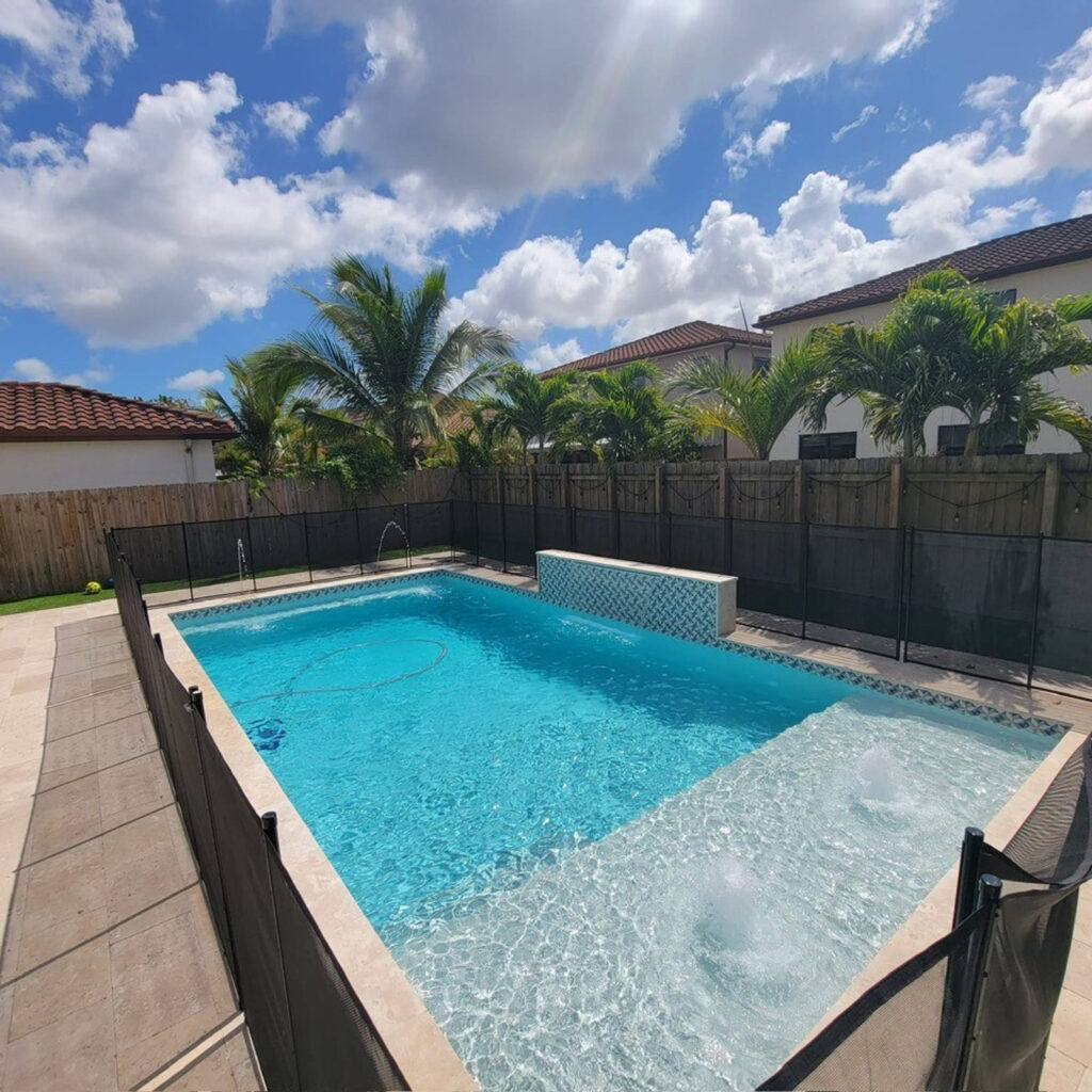 A small rectangular backyard pool with a raised spa water feature, bubbler jets, and a removable child-safety fence around the deck.