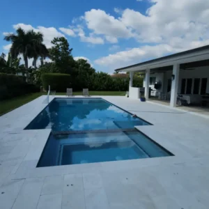 A rectangular pool with an attached spa on a travertine deck beside a covered patio.